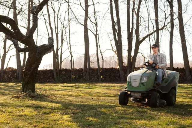 Man on a green riding lawnmower mowing a grassy yard, trees in background.