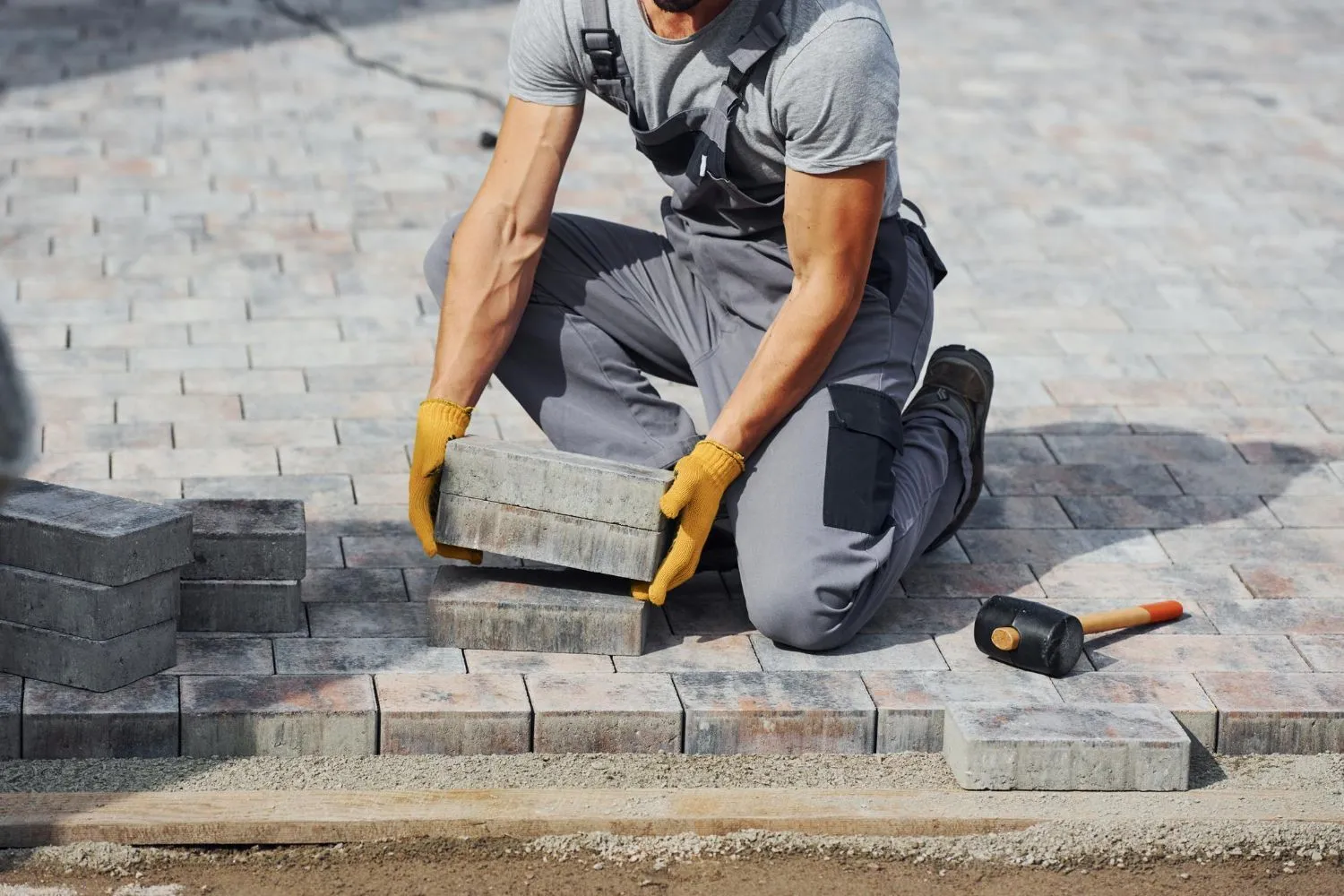 Man laying grey paving stones, wearing gloves, in an outdoor setting.
