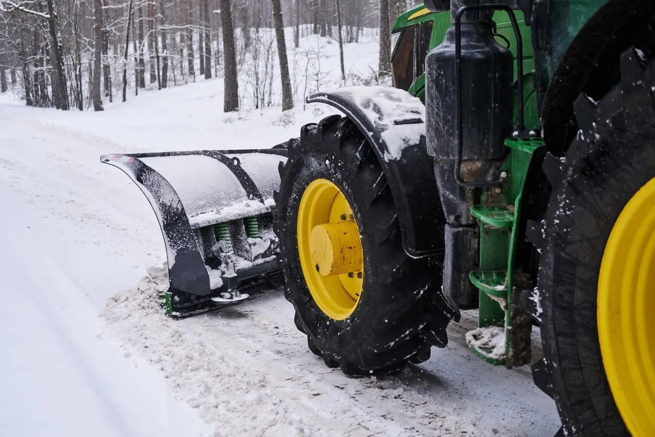 A green and yellow tractor plowing snow off a road.